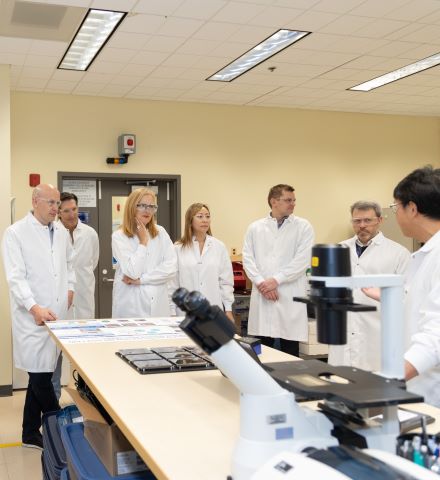 실험실에 있는 현미경 옆에 흰 실험실 가운을 입고 서 있는 사람들.